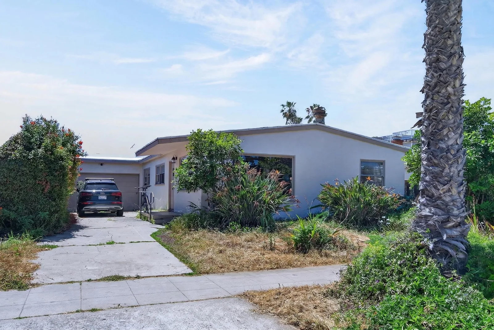 Front exterior not prepped — car in driveway, overgrown plants, clutter